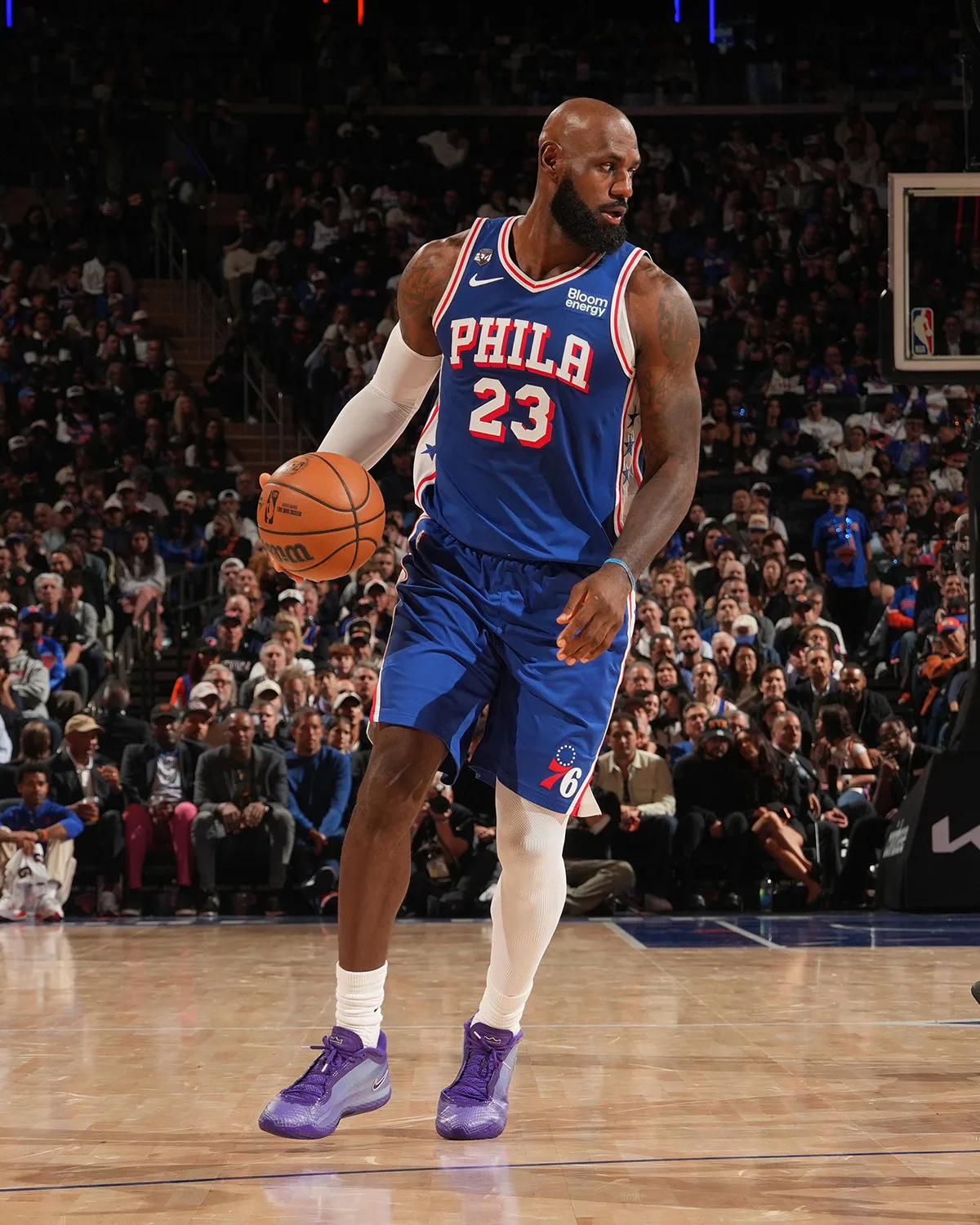 Player in blue Phila 23 jersey dribbling on hardwood, wearing purple sneakers, crowd behind, Opening Night