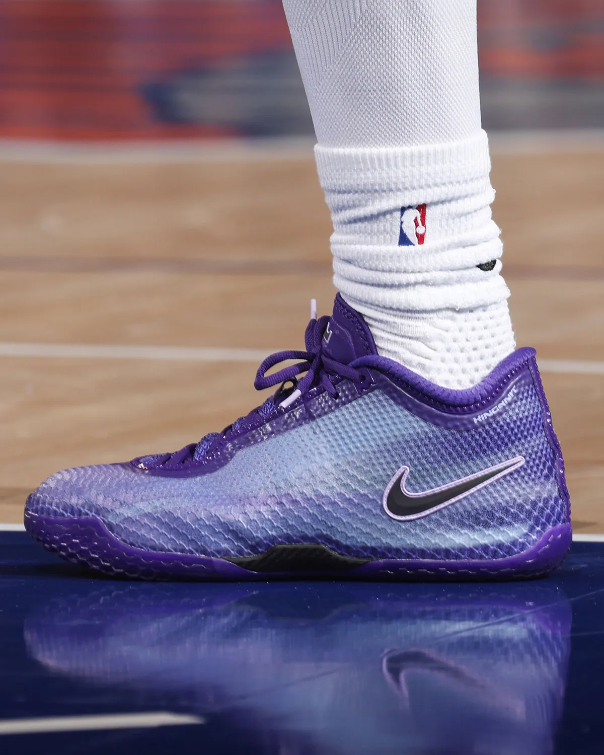 On-foot lateral view of purple sneaker with black swoosh and white NBA sock on hardwood, Nike LeBron 24 “Opening Night” PE
