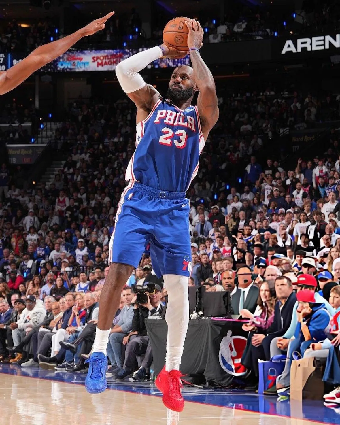 On-court jump shot in blue Phila 23 jersey, one blue and one red shoe, crowd behind, Philly