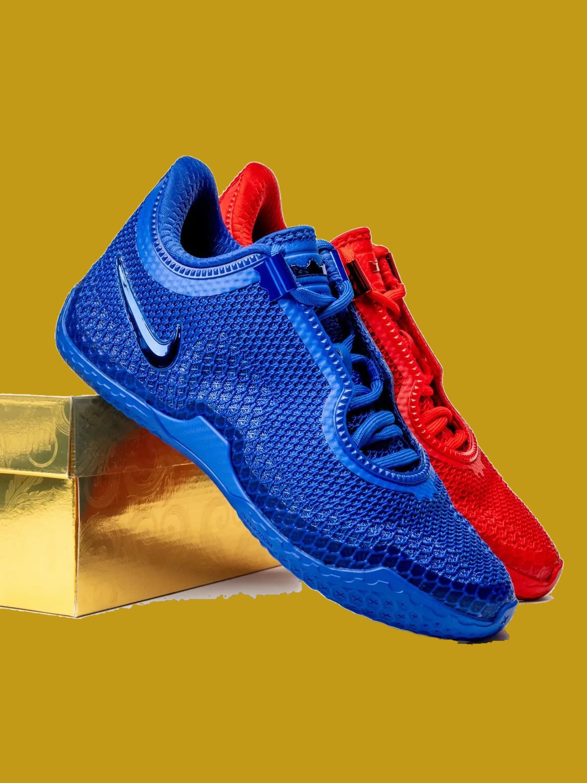 Blue and red pair angled on gold box edge, glossy blue swoosh, laces and strap visible, Philly