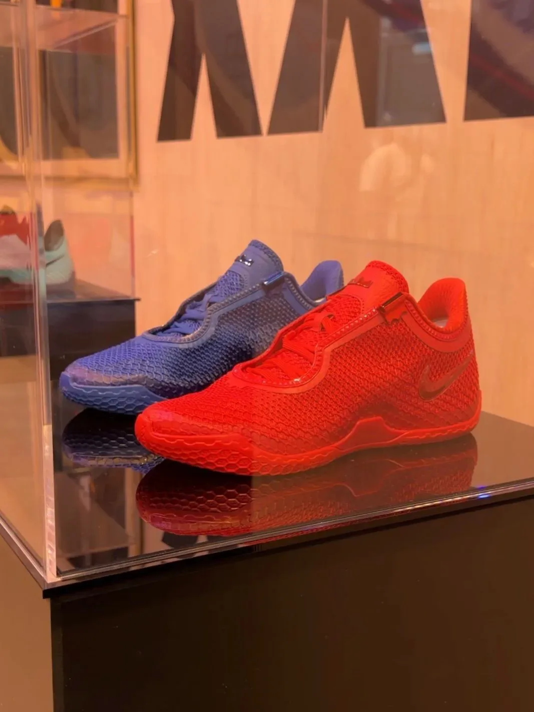 Pair in display case, red mesh shoe in front of blue, on black glossy plinth, Red and Blue