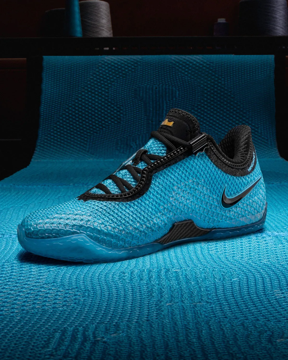 Lateral view of blue knit shoe with black laces and swoosh on a blue woven textile backdrop, Stars