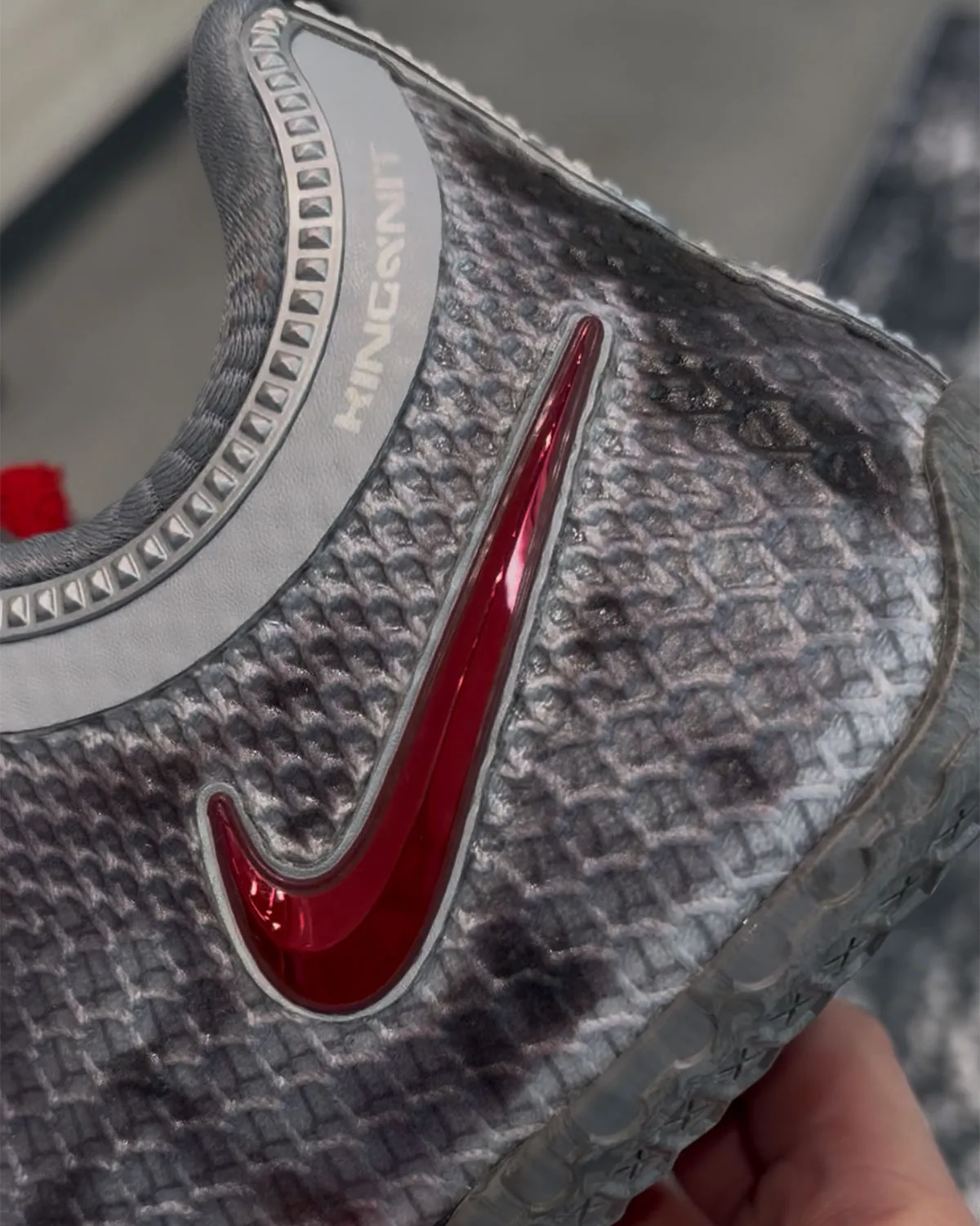 Close-up of red chrome swoosh on grey scaled mesh, studded collar trim and KINGSKNIT text, Storm Drain