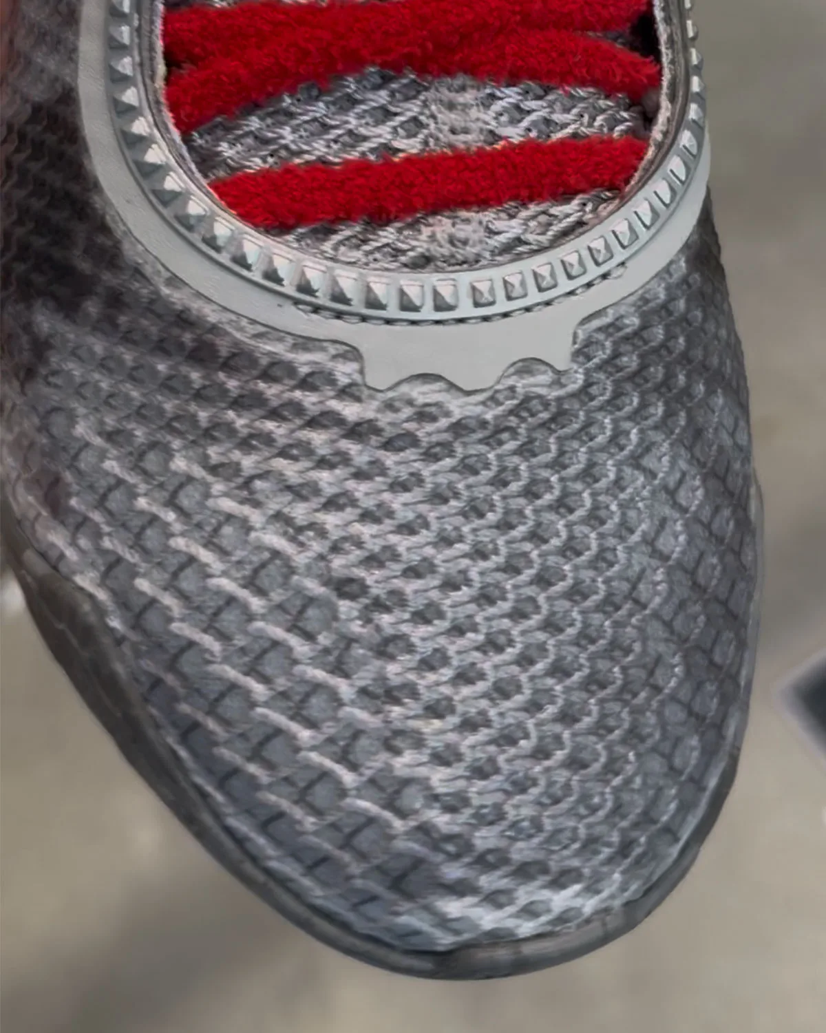 Toe box close-up of grey scaled textured upper, studded trim and fuzzy red laces at top, Storm Drain