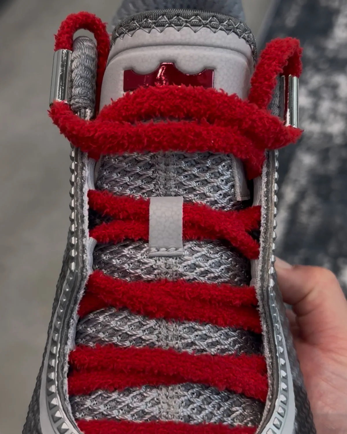 Top-down close-up of fuzzy red laces over grey knit tongue, silver lace tips, red crown logo, Storm Drain