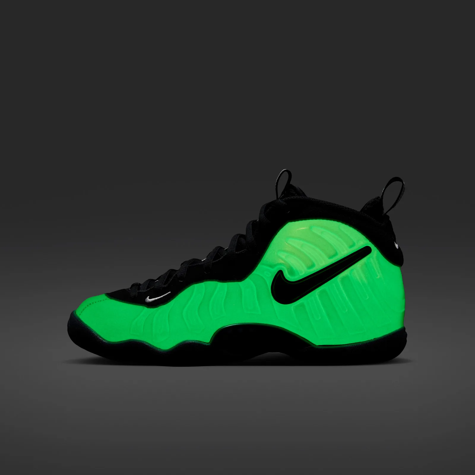 Lateral view glowing bright green in the dark, black swoosh and laces on grey background, Glow In The Dark