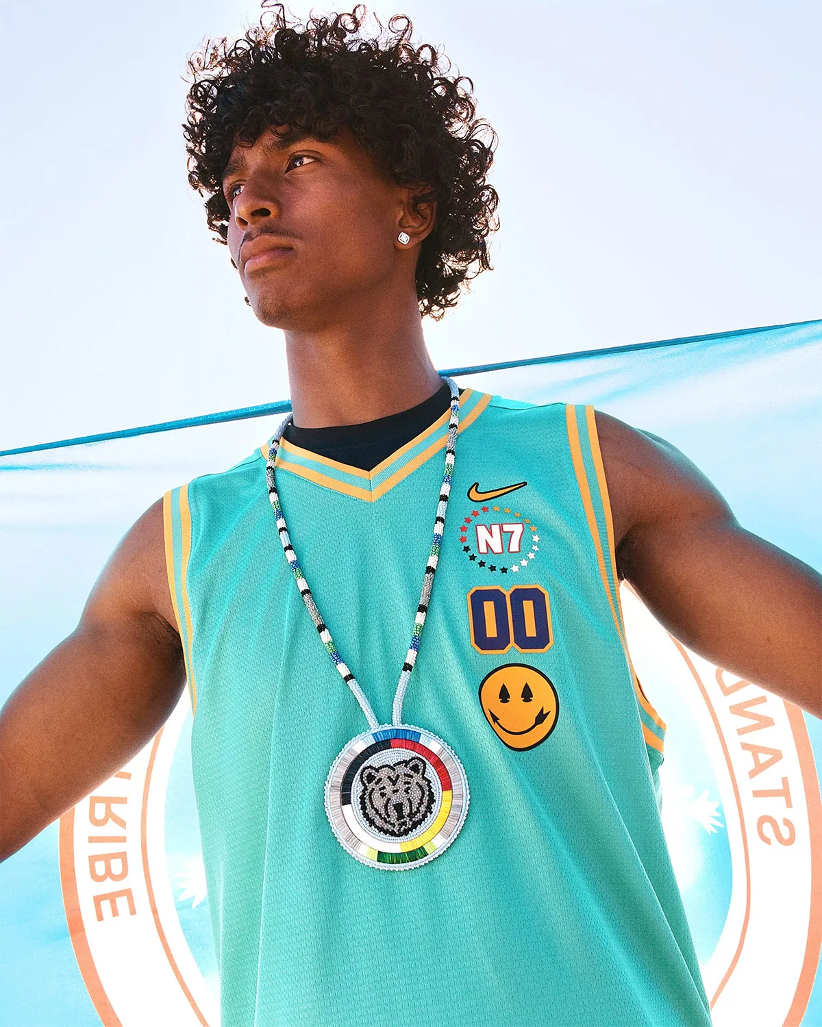Low-angle portrait of young man in teal jersey with N7 and 00, beaded bear medallion necklace, Holiday 2026 Collection