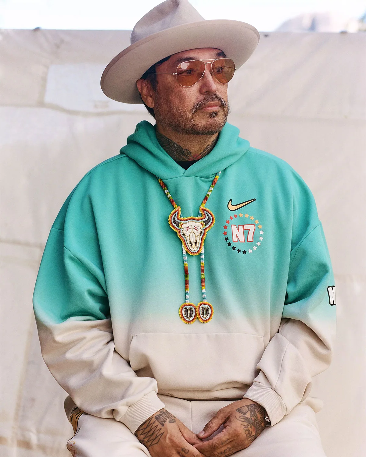 Portrait of man in wide-brim hat, teal-to-cream hoodie with N7 logo, beaded bull skull necklace, Holiday 2026 Collection