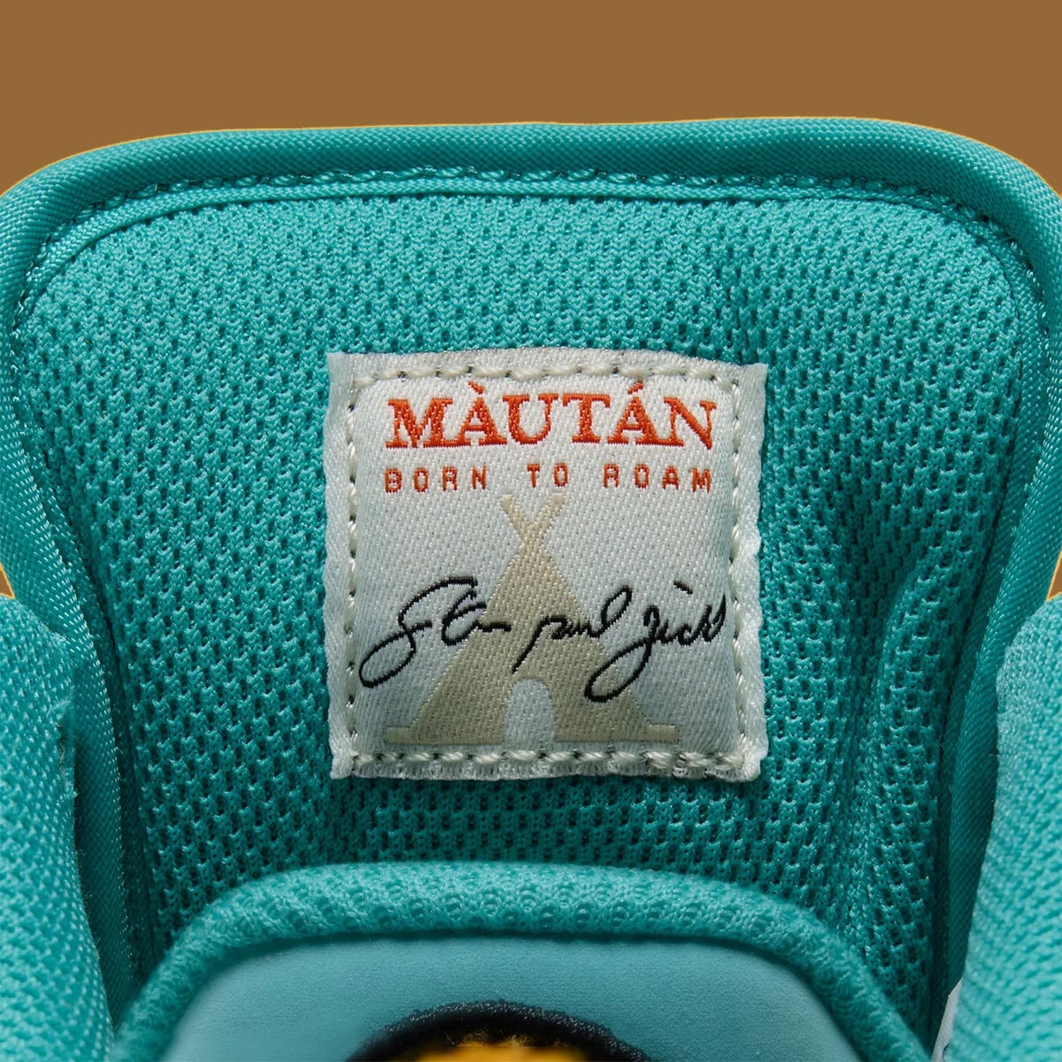 Inner tongue label on teal mesh, orange text 'Màután Born to roam', tipi graphic, signature, Holiday 2026 Collection