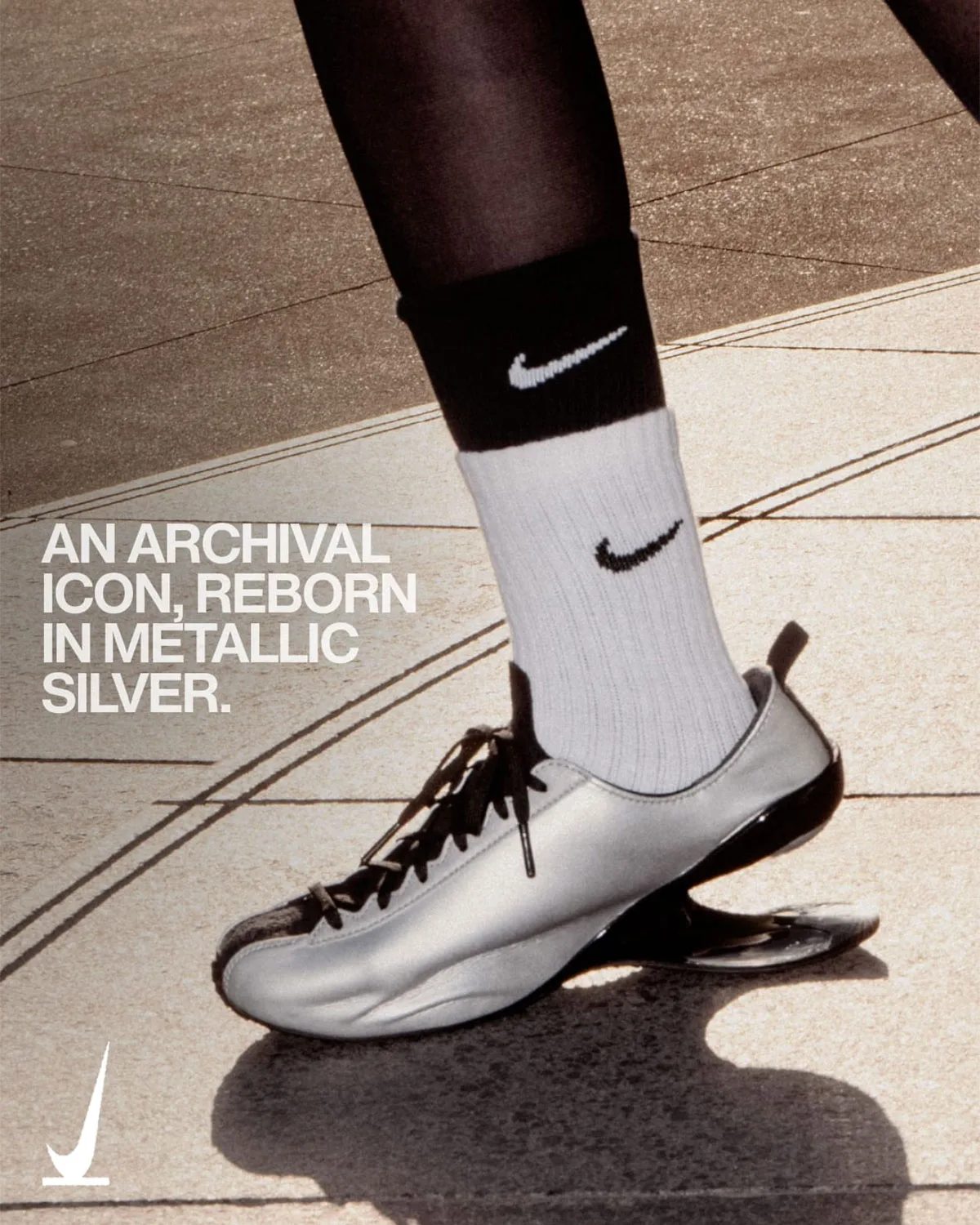 On-foot lateral view of silver shoe with white Nike sock on paving, text 'An archival icon, reborn in metallic silver', Nike