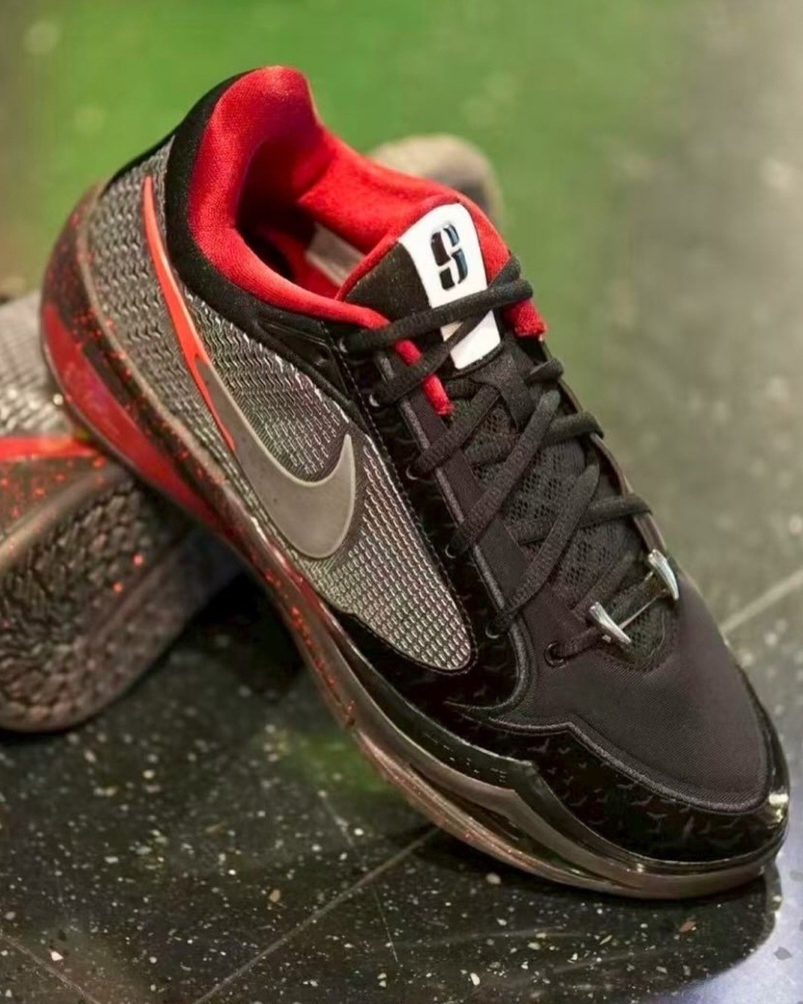 Angled front view on a speckled floor, black and grey upper, red collar lining, white tongue label, Halloween