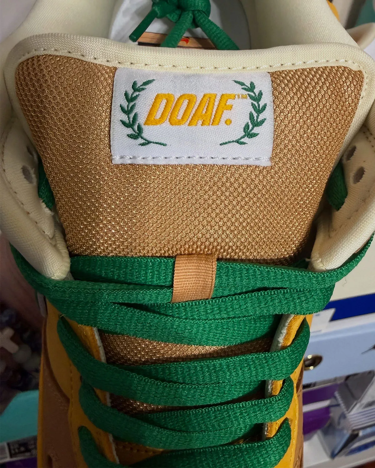 Top-down tongue detail, DOAF label with laurel wreath on tan mesh, green laces, Shout