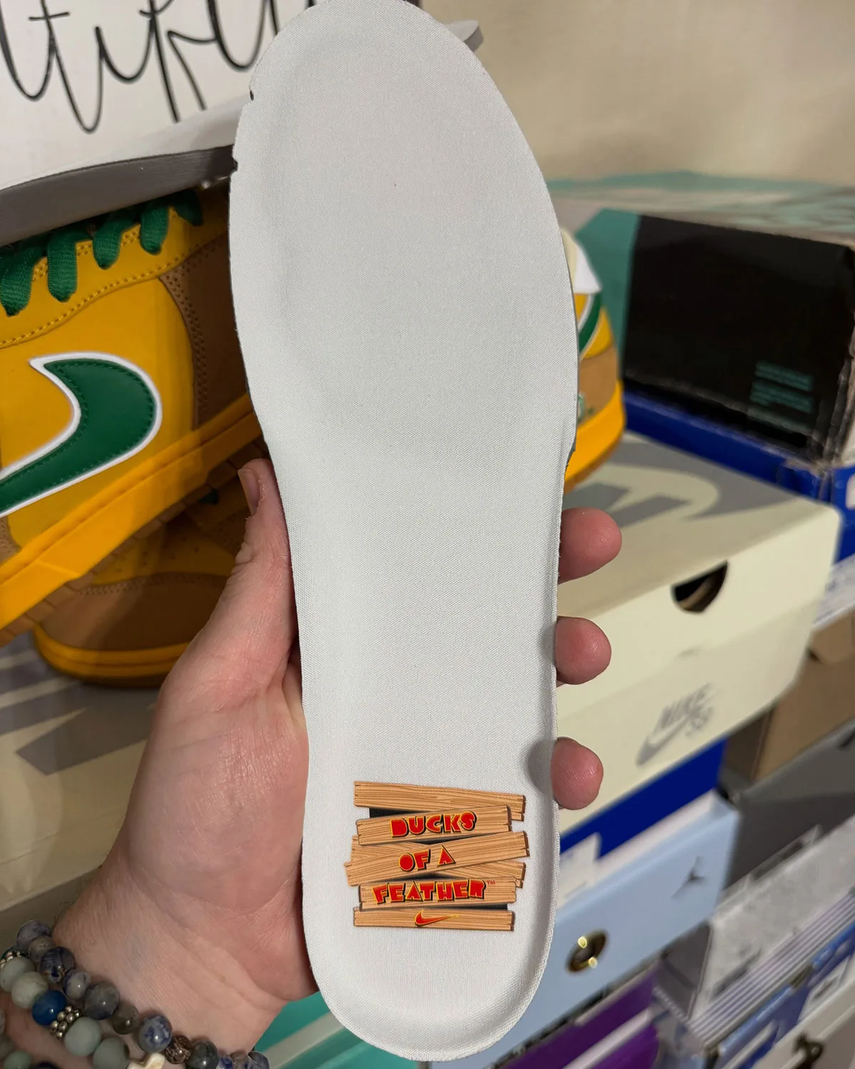 In-hand white insole with Ducks of a Feather wood-plank graphic, shoe behind, Shout