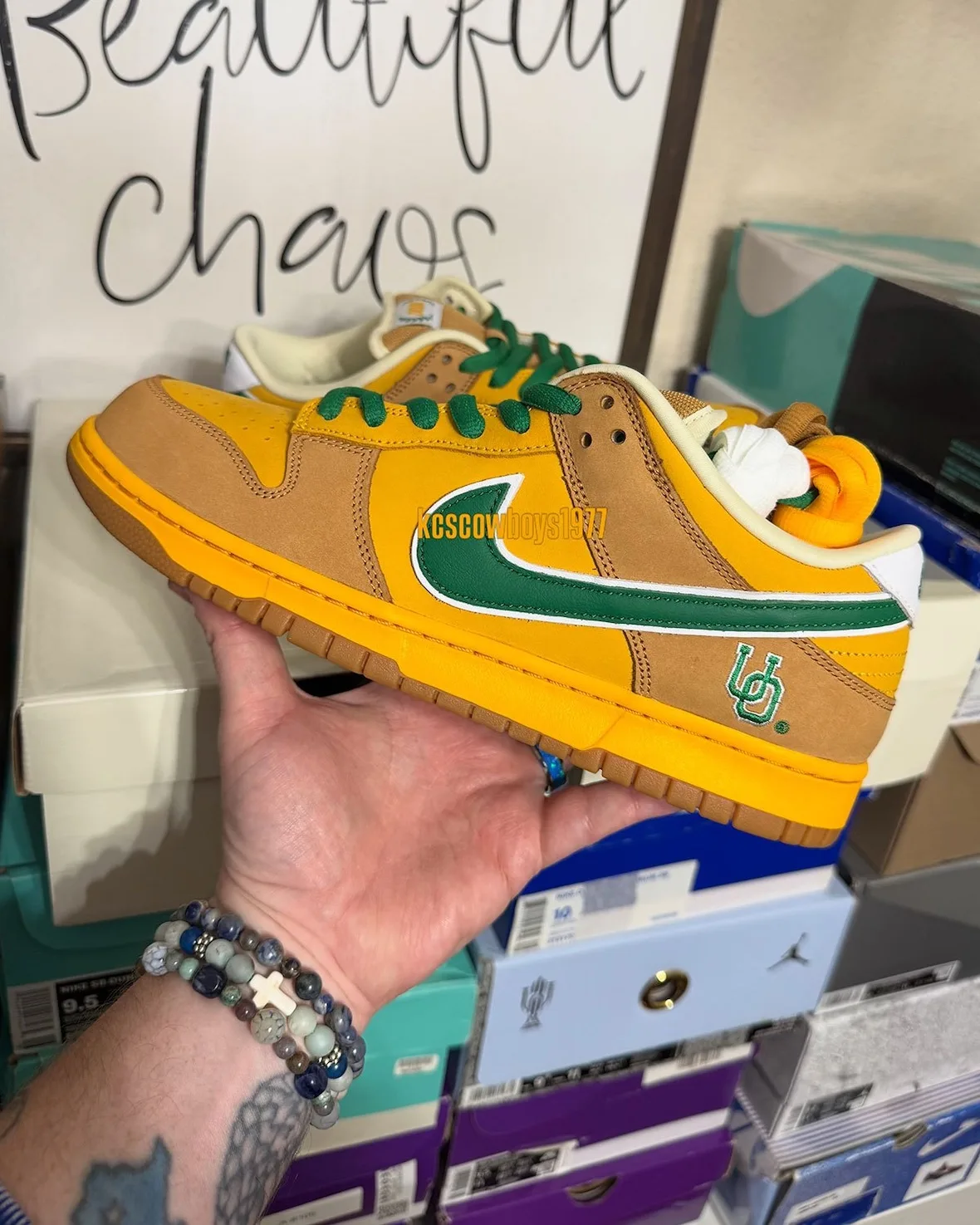 Lateral in-hand view, yellow and tan upper, green swoosh, UO logo, shoe boxes behind, Shout