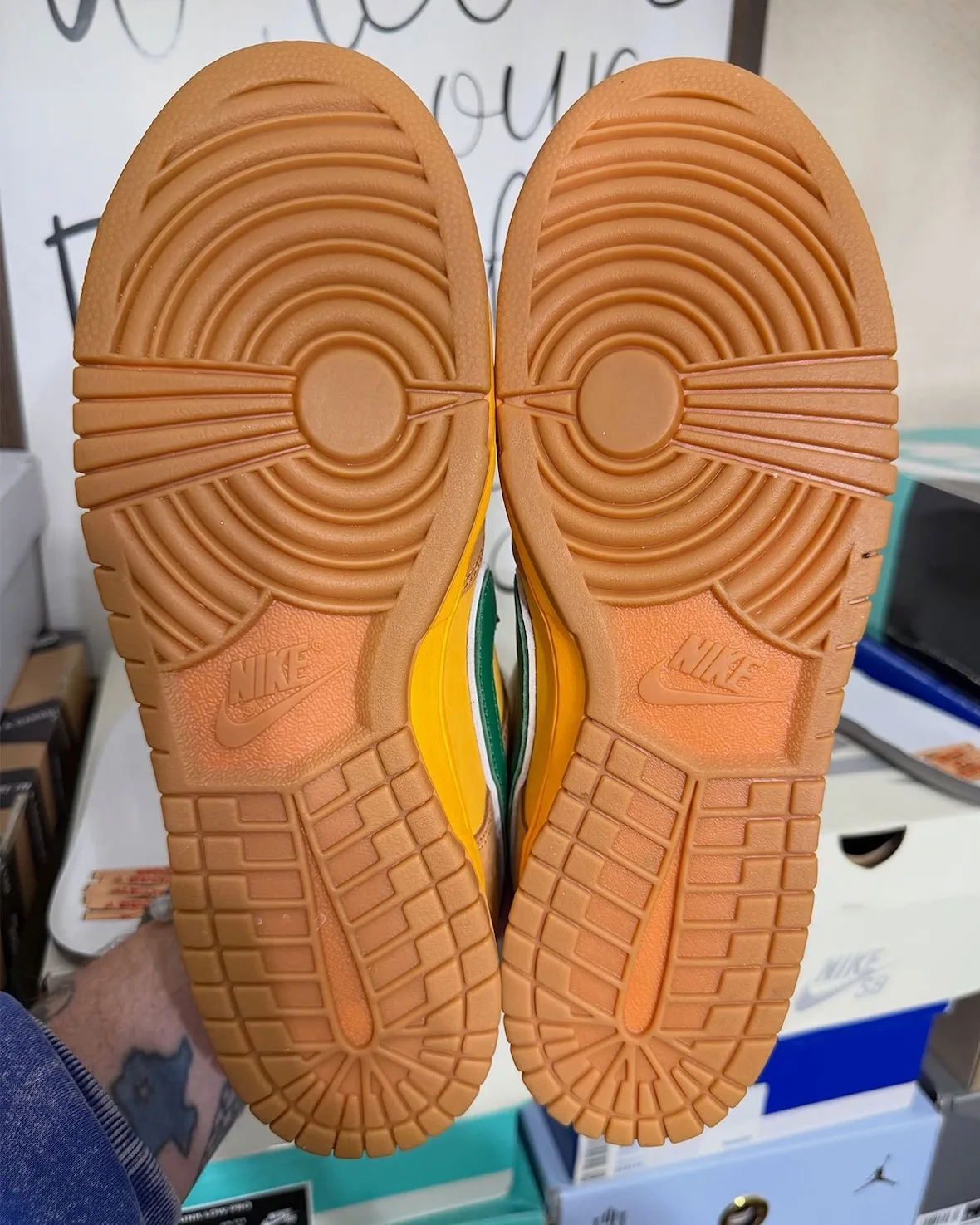 Outsole view of pair, gum rubber with circular pivot pattern and orange Nike logos, Shout