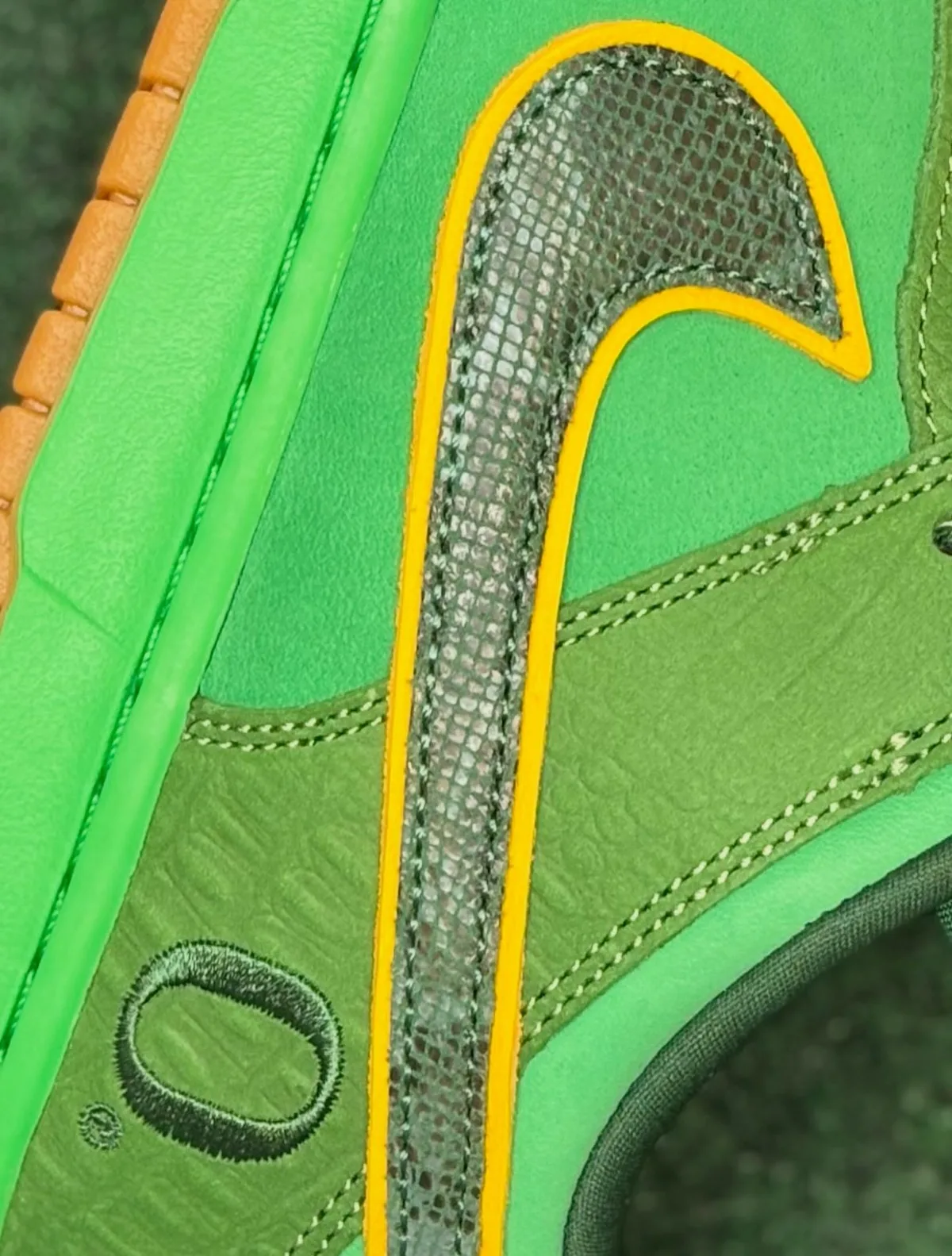 Detail of green shoe side: dark snakeskin-textured swoosh with yellow trim, embroidered O, The Zoo