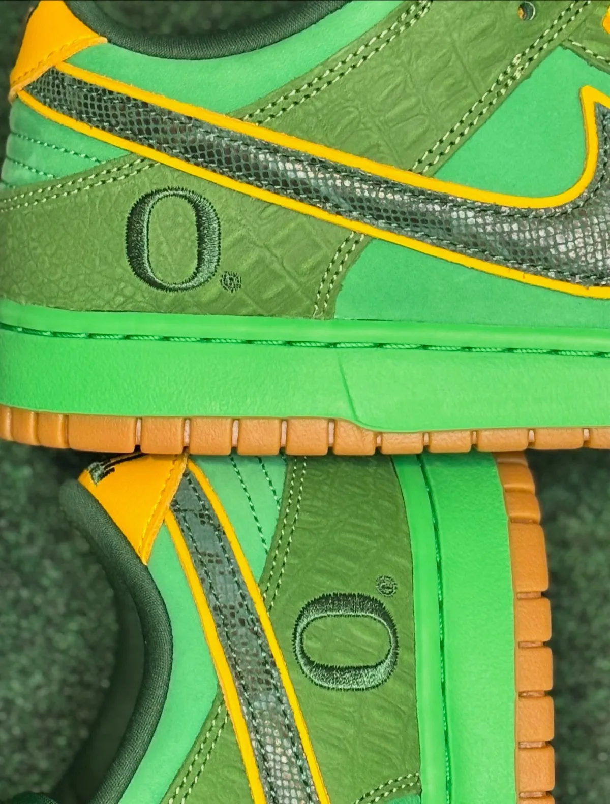 Lateral detail of two shoes: embroidered O on croc-textured green panel, snakeskin swoosh, The Zoo