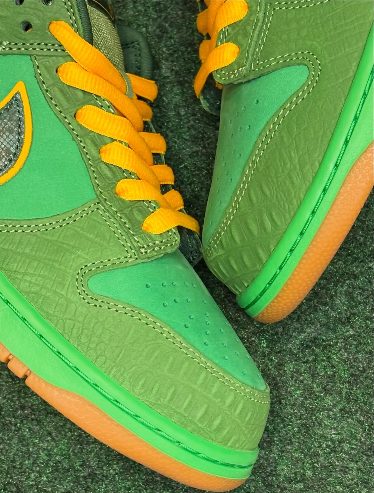 Toe detail of green croc-textured shoes with yellow laces and gum sole on green turf, The Zoo