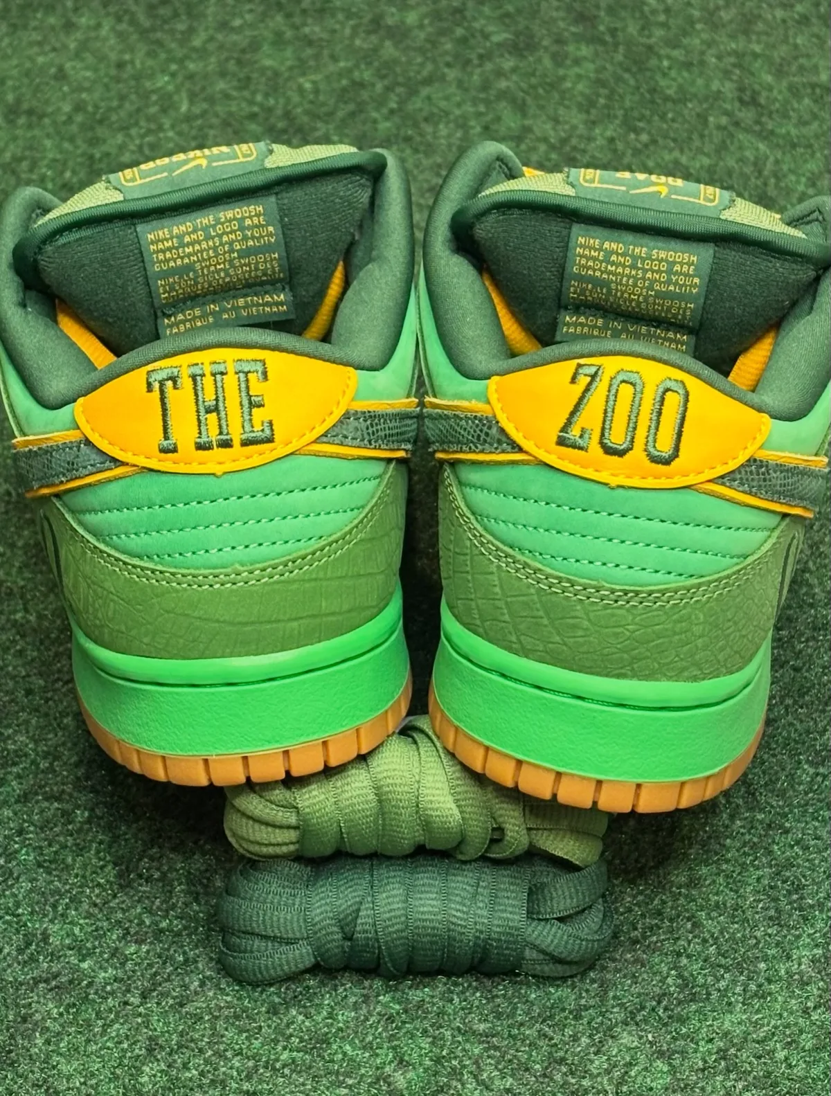 Heel view of pair with yellow tabs reading THE ZOO, croc-textured green panels, gum soles, The Zoo