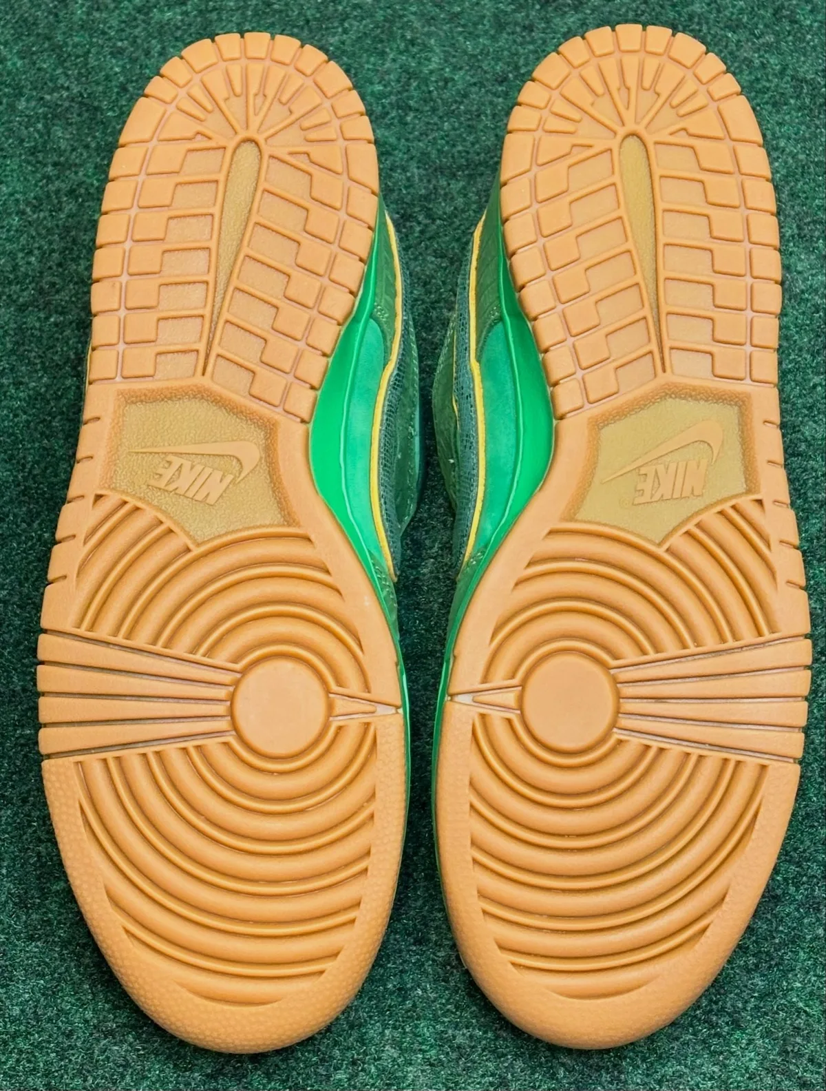 Outsole view of pair: gum rubber with circular and herringbone tread, Nike logo on each, The Zoo