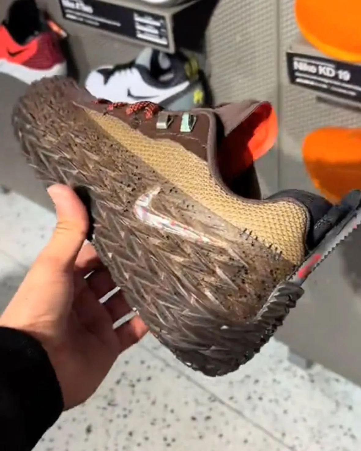 In-hand shoe tilted showing spiky speckled sole, Swoosh and store display behind, Halloween