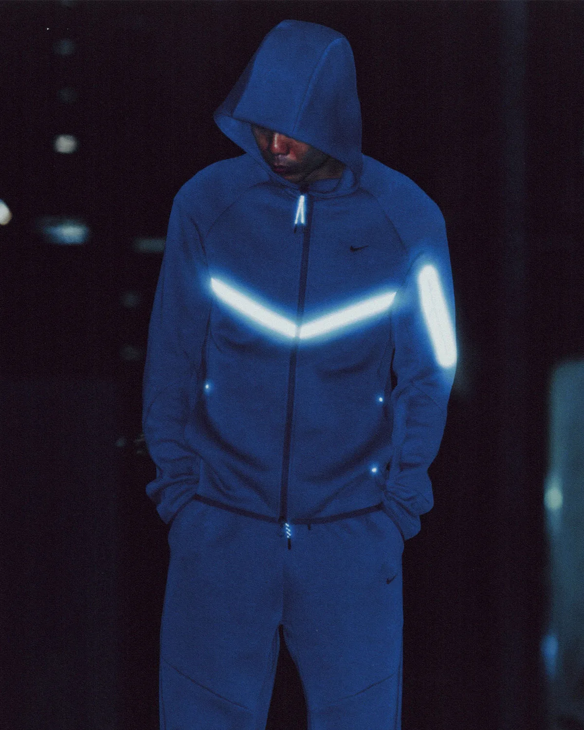 Night on-foot shot, blue hooded zip jacket with glowing chevron and sleeve stripe, Boreas and SF3