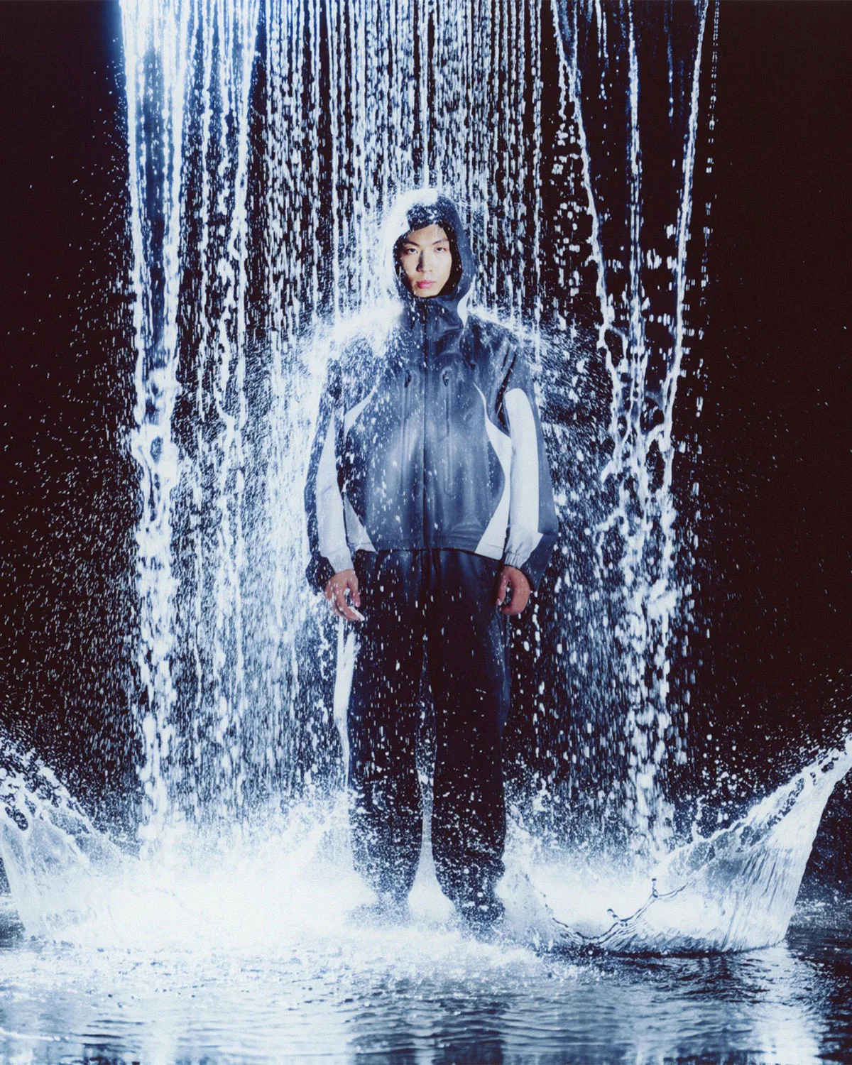 On-foot shot of person in grey and navy hooded jacket standing under a waterfall, Boreas and SF3