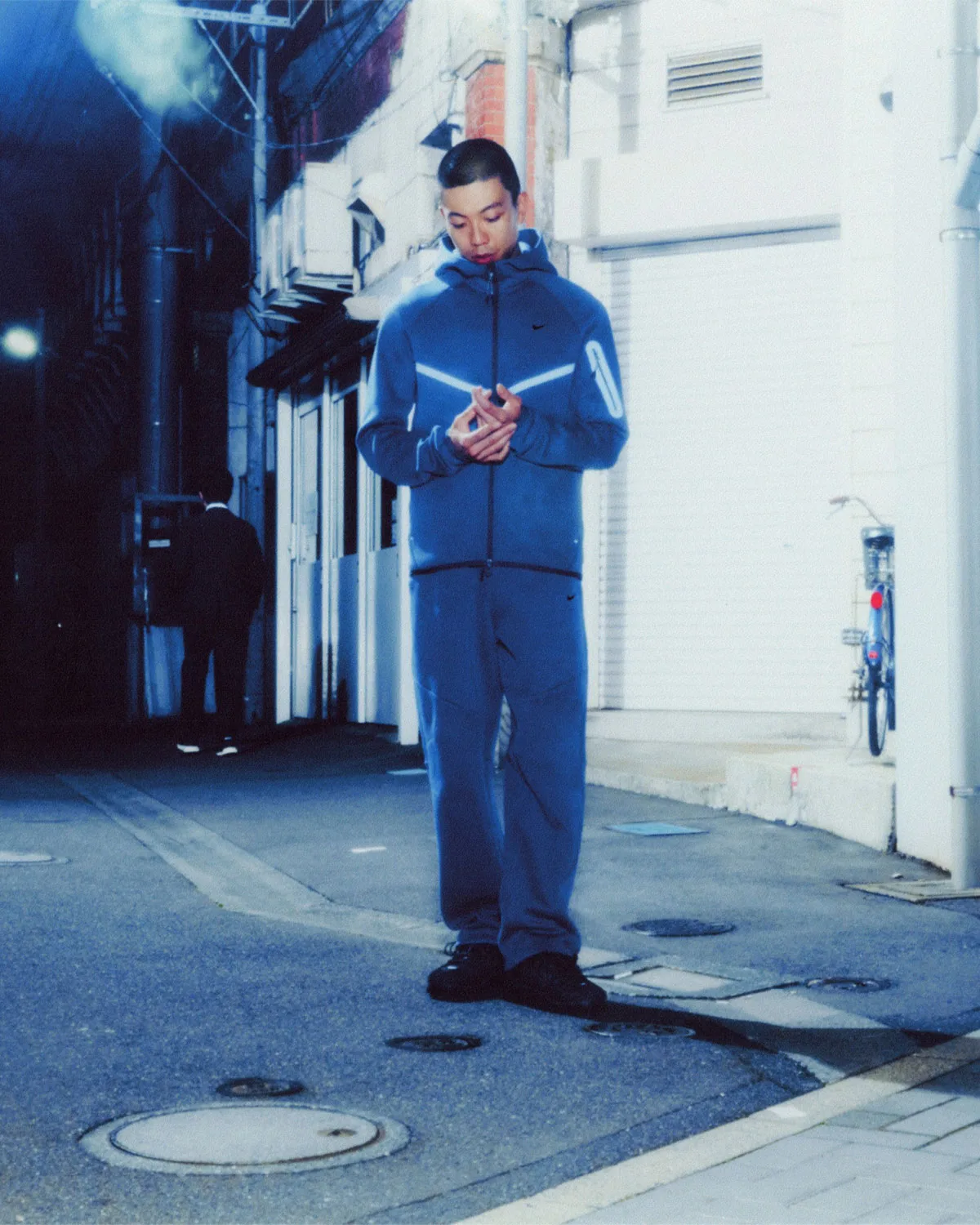On-foot street shot at night, blue hoodie with reflective chevron, bicycle by white wall, Boreas and SF3