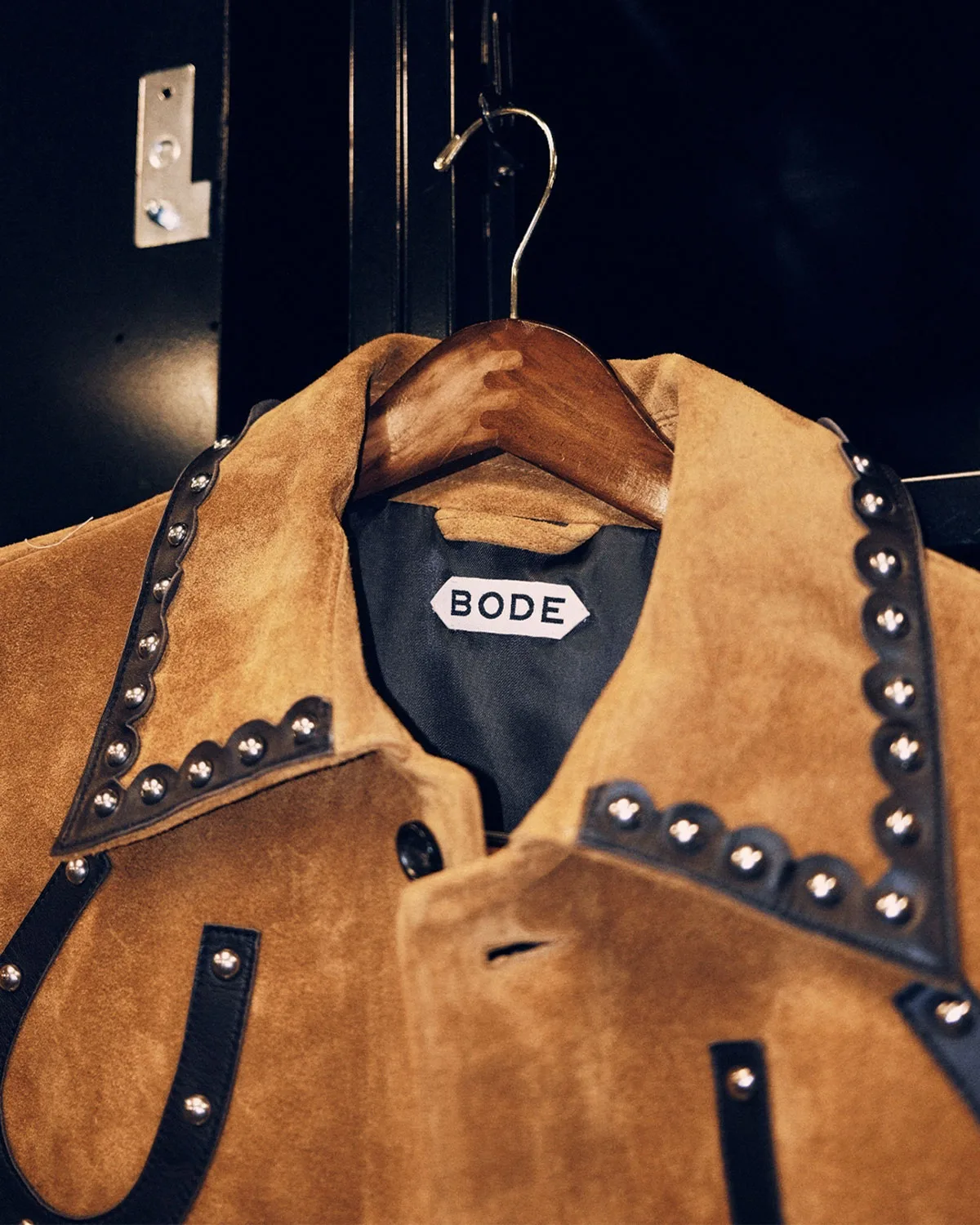Detail of tan suede jacket on a hanger with studded black collar trim and Bode label, Vapor Pro 1