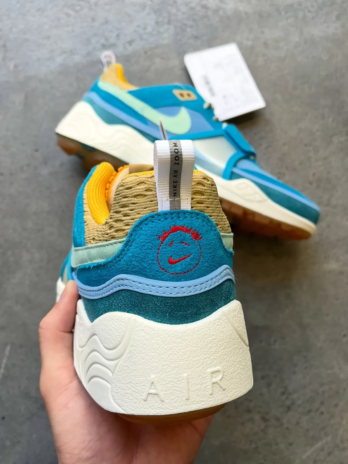 Heel view in hand: red smiley stitching, white AIR lettering on cream midsole, Blue