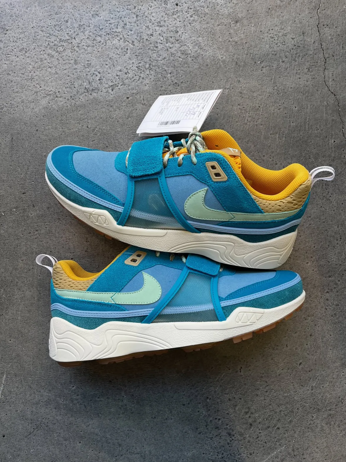 Pair of blue and teal sneakers, lateral view, mint swooshes, cream midsoles, hang tag, Blue