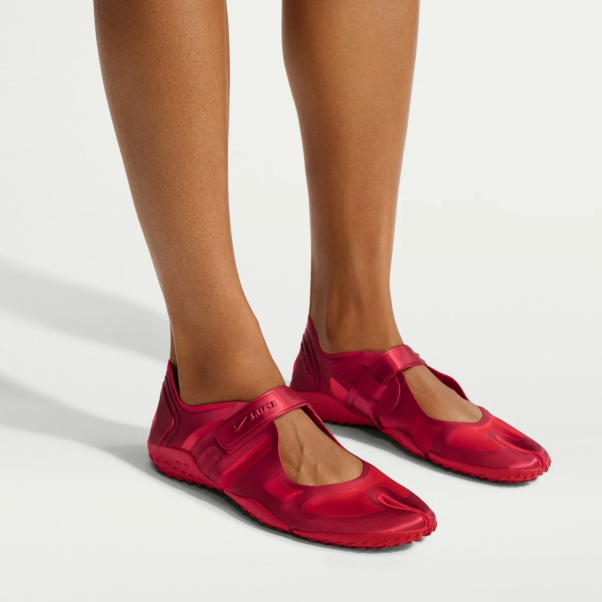 On-foot, tan legs in red satin split-toe shoes with strap, white backdrop, University Red