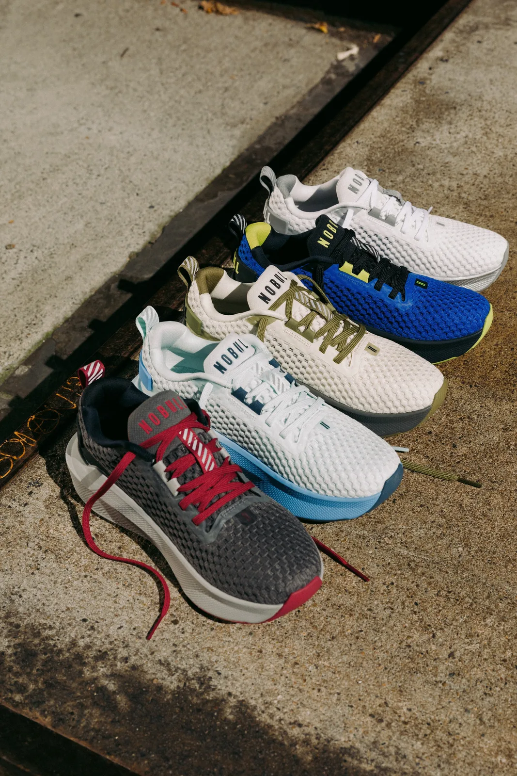 Five colourways lined up on concrete: grey and red, white and blue, olive, royal blue, white, NOBULL Journey 2