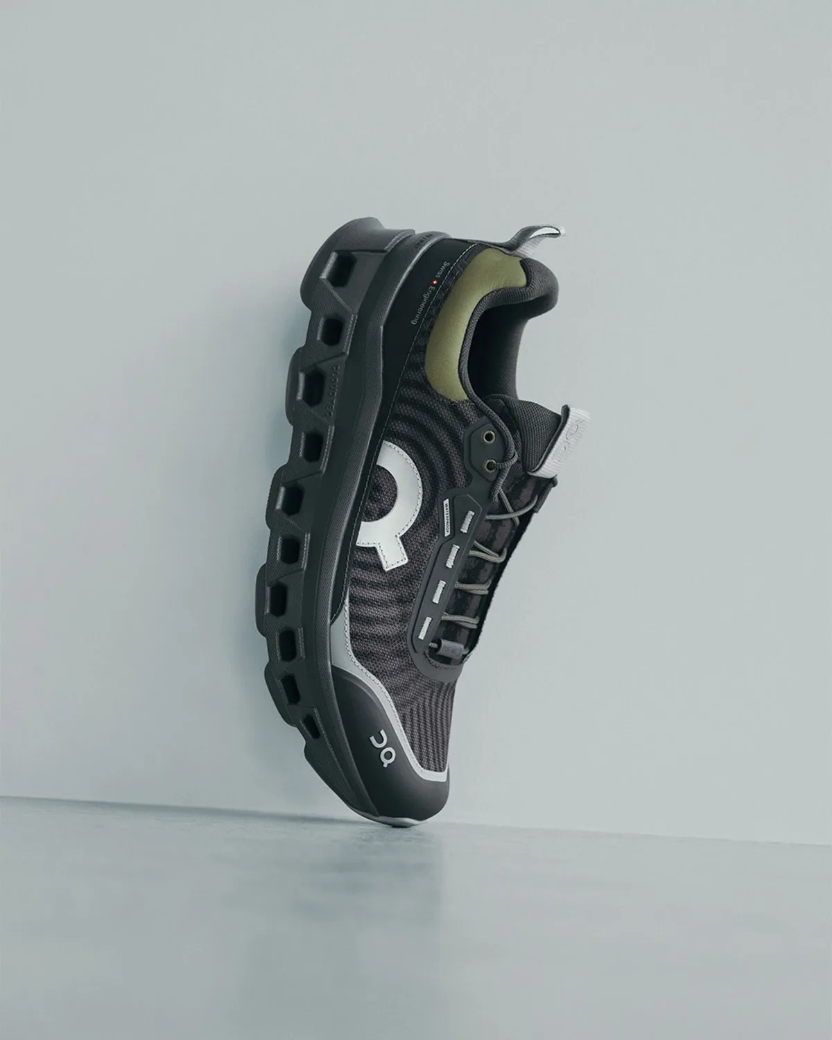 Lateral view of black sneaker leaning on a pale wall, olive heel patch, silver logo, WP x atmos