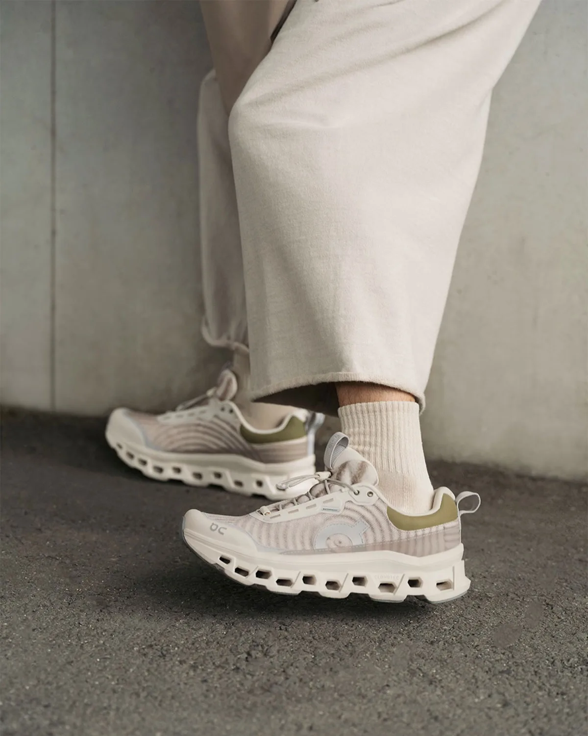 On-foot pair in cream and beige with olive heel patch, cream trousers, concrete wall, WP x atmos