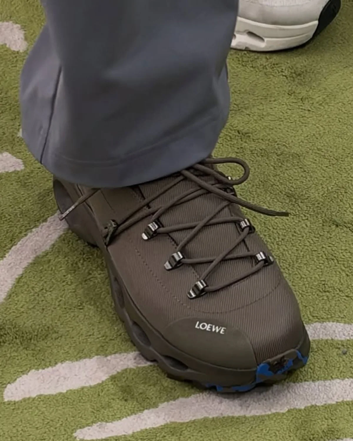 On-foot front three-quarter view, brown ribbed upper, metal lace hooks, LOEWE toe cap, green rug, Hiker x Loewe