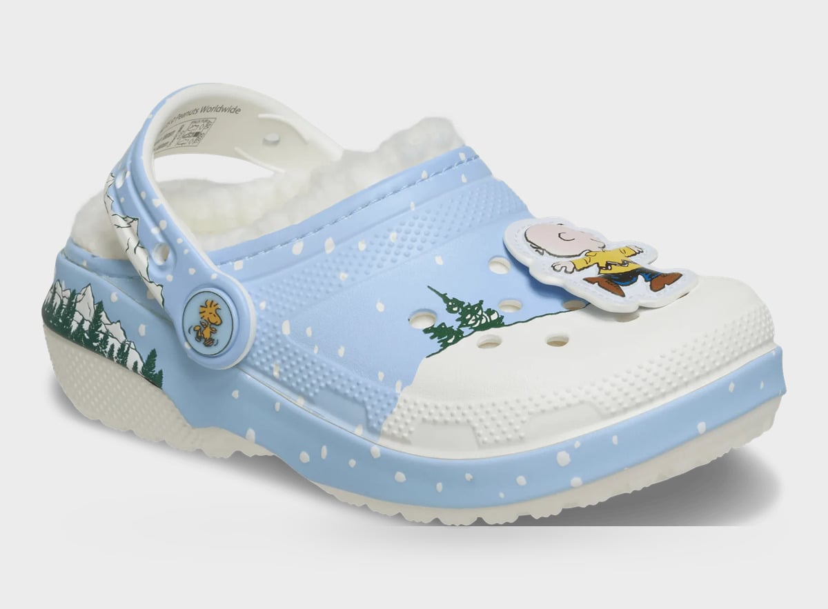 Three-quarter view of light blue clog with white toe, boy in yellow shirt charm, green pines, Classic Lined Clog