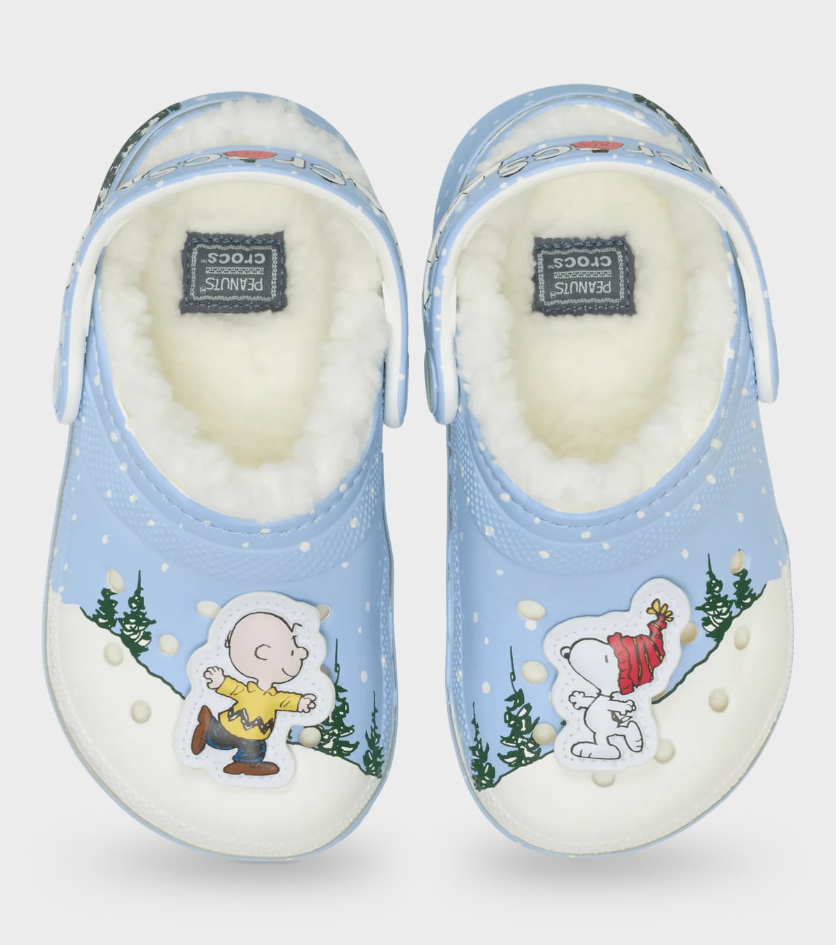 Top-down view of light blue and white clog pair, fleece insoles, charms, green pines on a snowy scene, Classic Lined Clog