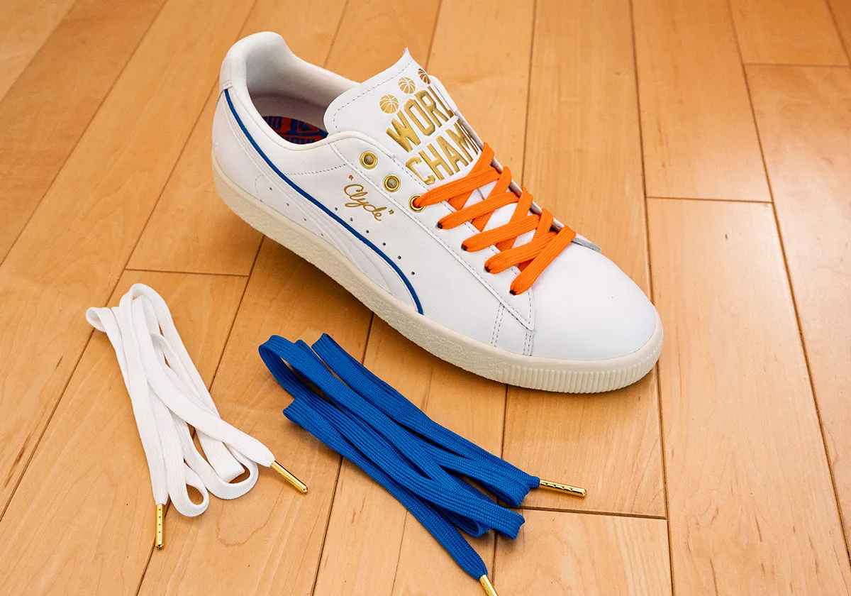 White sneaker with orange laces and gold tongue text, beside spare white and blue laces with gold tips, Ceremony