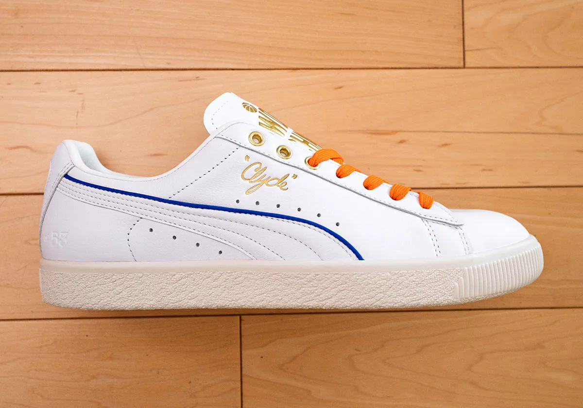 Lateral view of white sneaker with blue stripe, gold script "Clyde", orange laces and cream sole, Ceremony