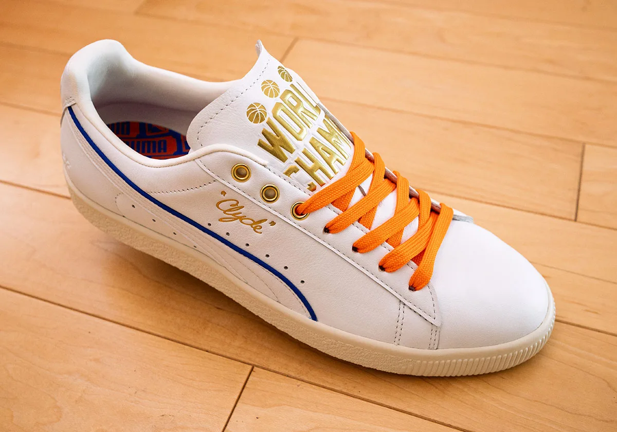 Three-quarter view of white sneaker with gold "World Champs" tongue text, orange laces, blue stripe, Ceremony