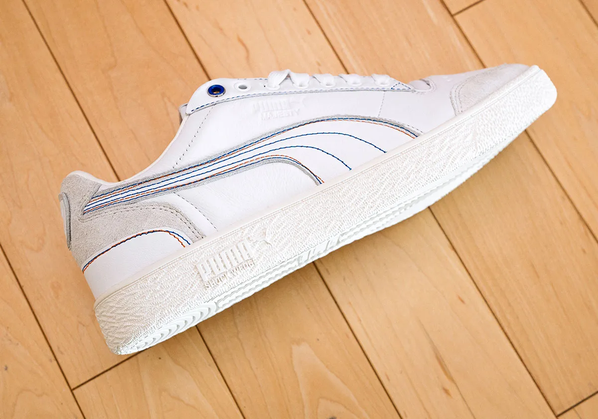 Low angled lateral view of white sneaker with cream sole, blue eyelet, blue and orange stitching, Ceremony