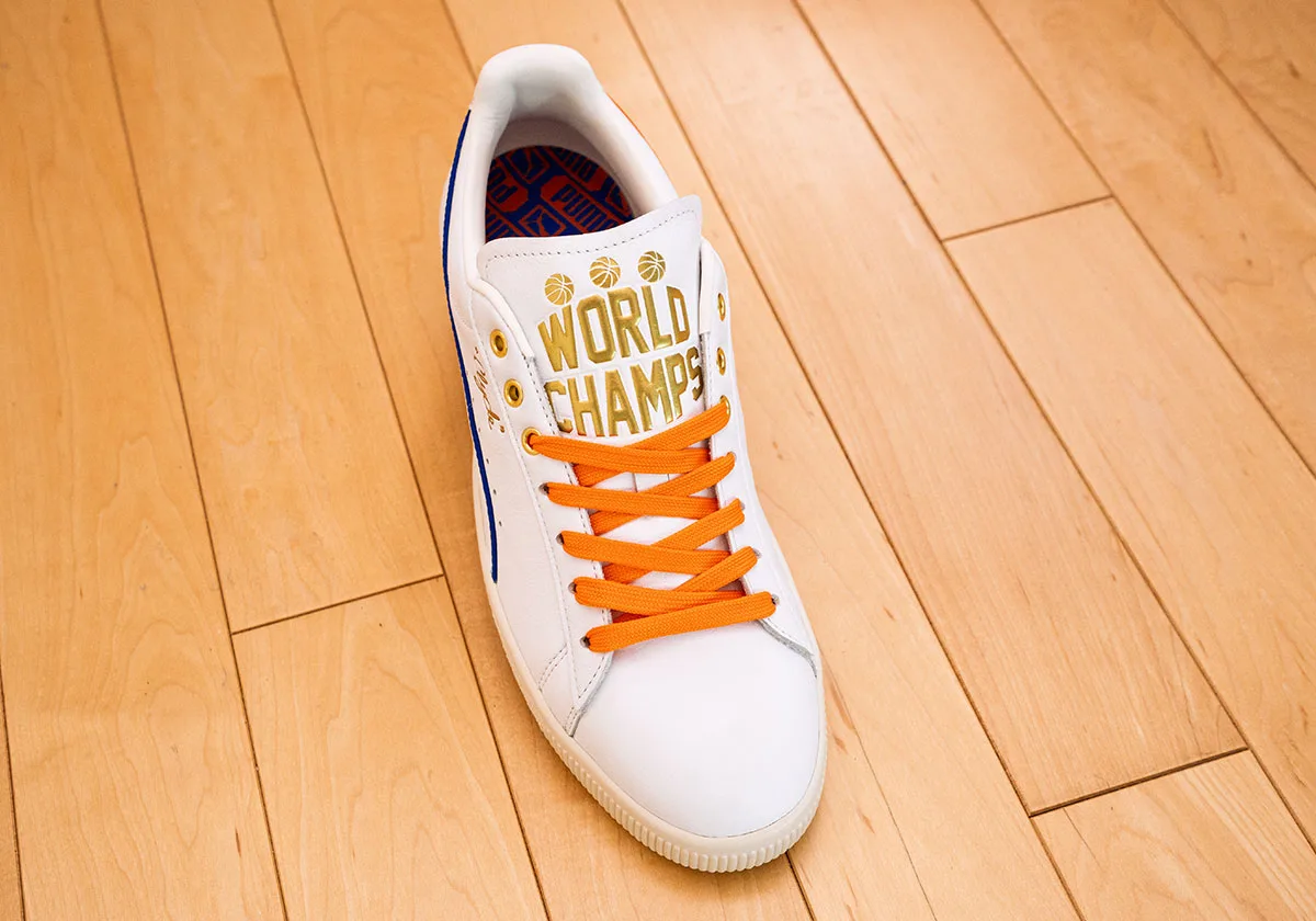 Top-down view of white sneaker with gold "World Champs" tongue text, orange laces and blue and orange insole, Ceremony