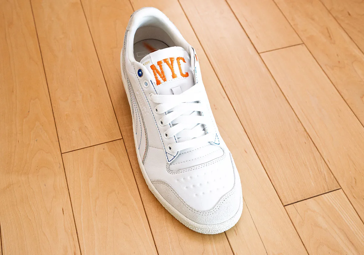 Top-down view of white sneaker with orange NYC embroidered tongue, white laces, grey suede toe, Ceremony