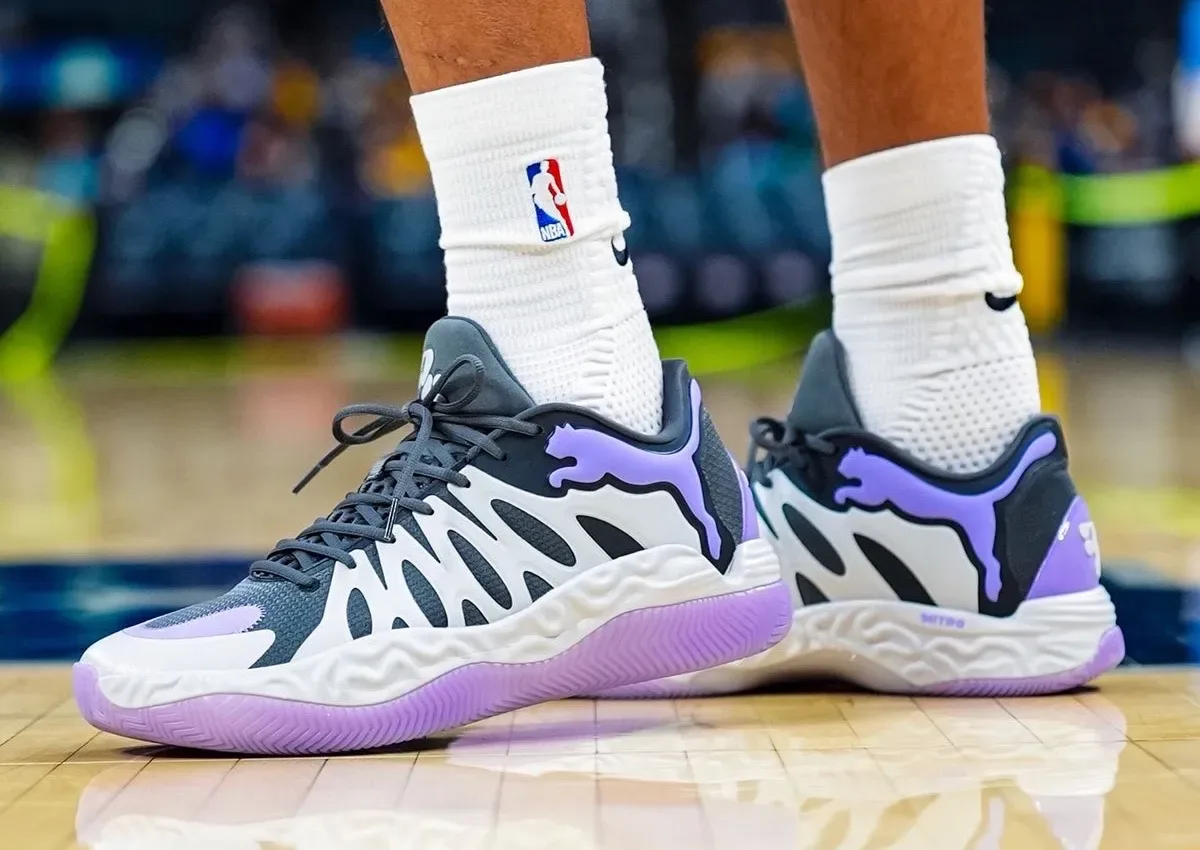On-foot pair on a hardwood court, purple PUMA cat logos, lilac outsole, white NBA socks, Teddy Lockart