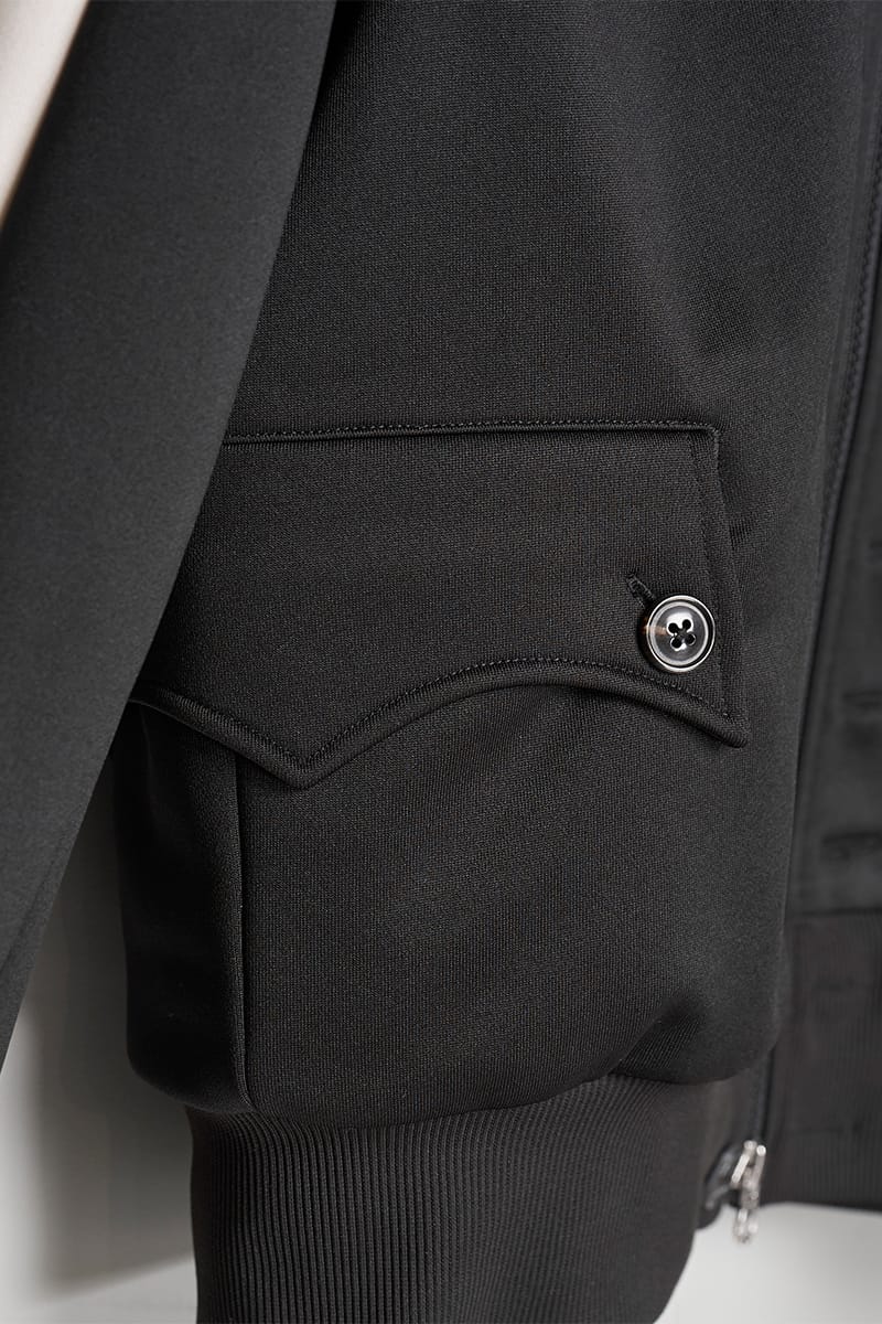 Close-up of black jacket flap pocket with horn-style button and ribbed hem, IVORYxBLACK