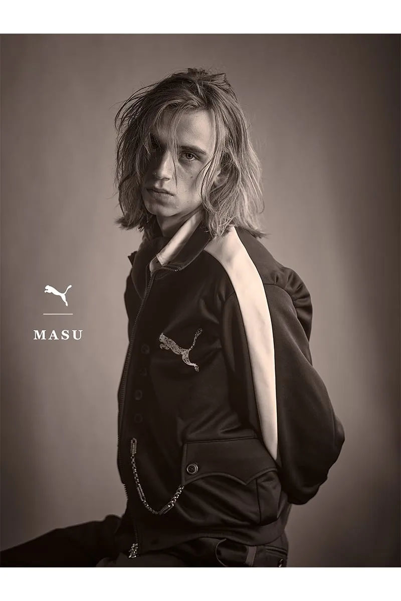 Sepia studio portrait of long-haired model in black track jacket, PUMA MASU logo at left, IVORYxBLACK