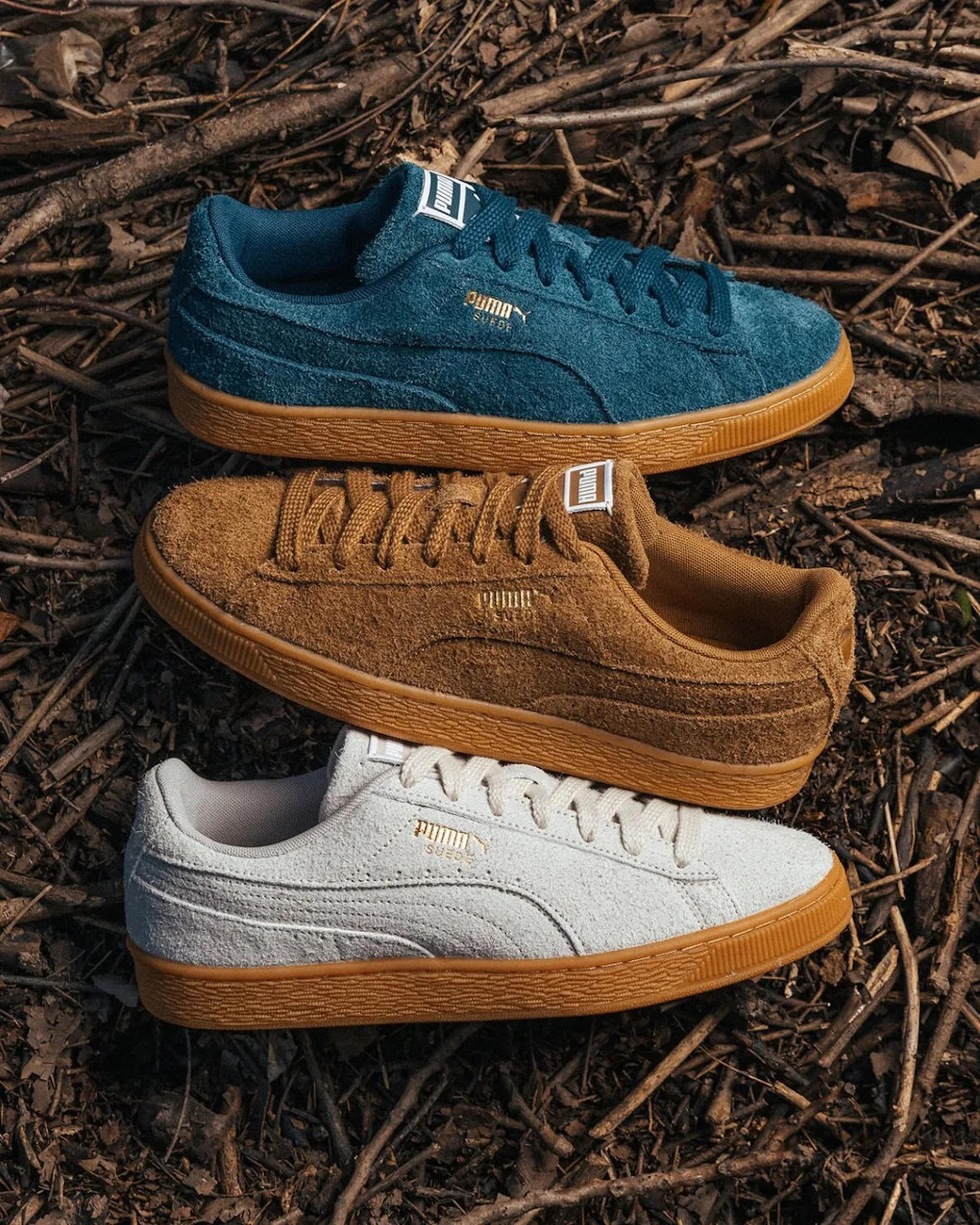 Three suede sneakers stacked on twigs in teal, brown and off-white, Forever
