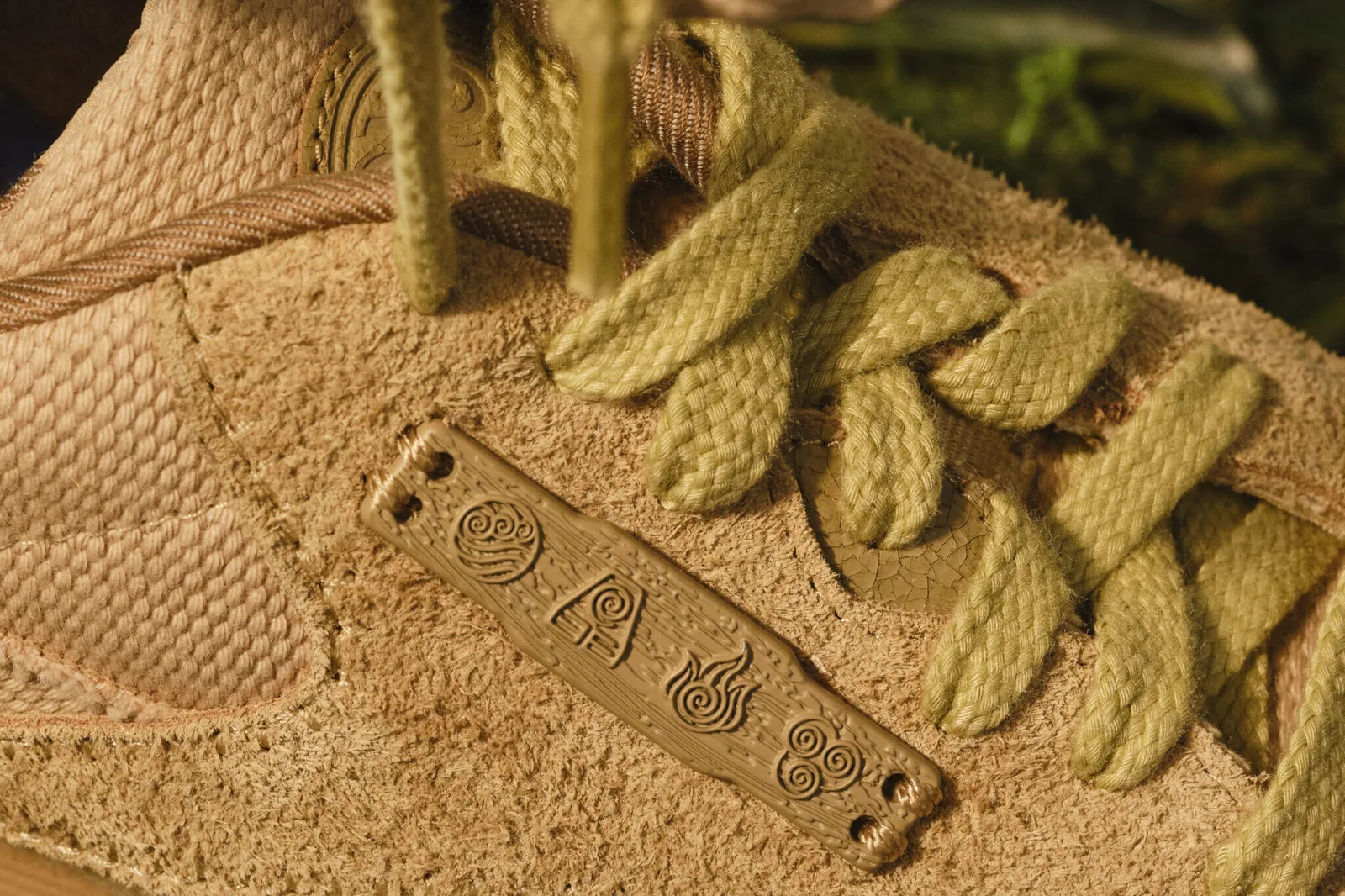 Close-up of the tan suede upper, olive laces and a carved plate with four element symbols, Four Nations