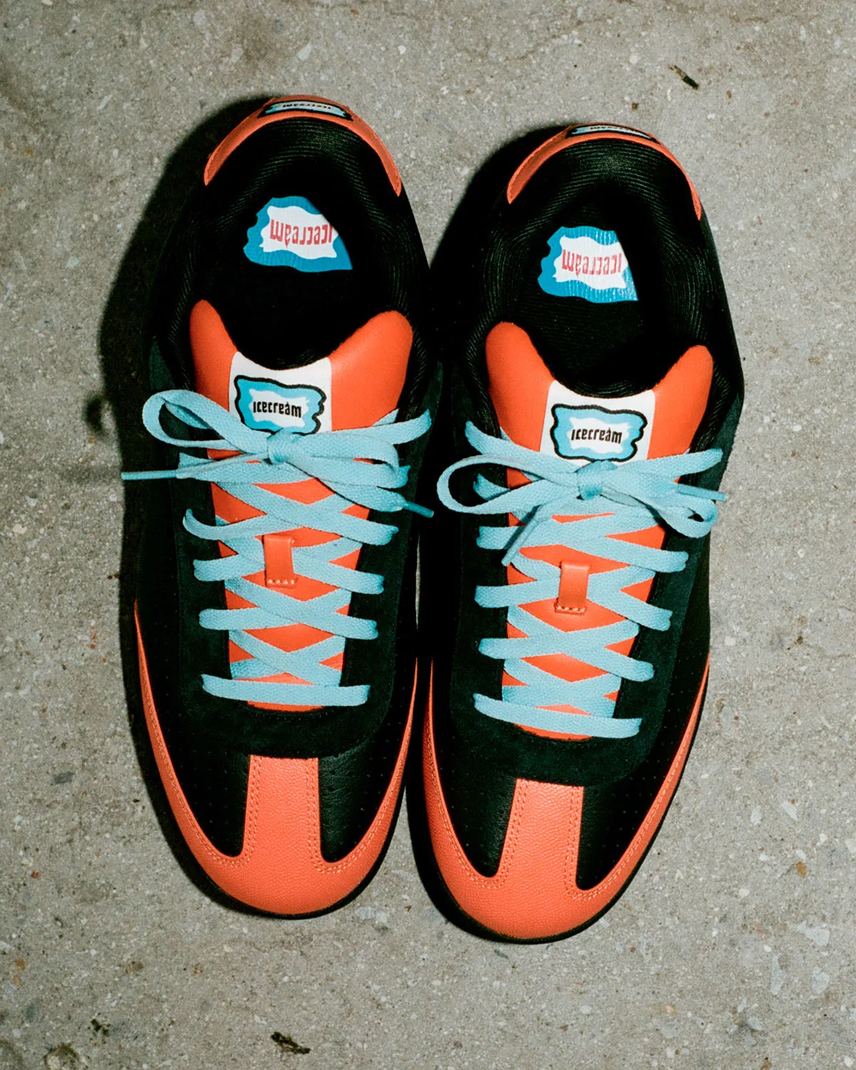 Top-down pair on concrete, black suede and orange toe caps, light blue laces, icecream tongue labels, Pumpkin
